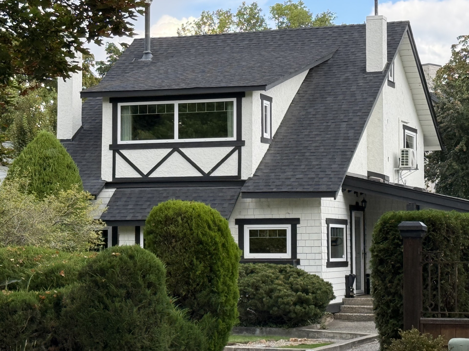 White house at 1923 Abbott Street in Kelowna with dark trim, a broad dormer window and established garden shrubs.