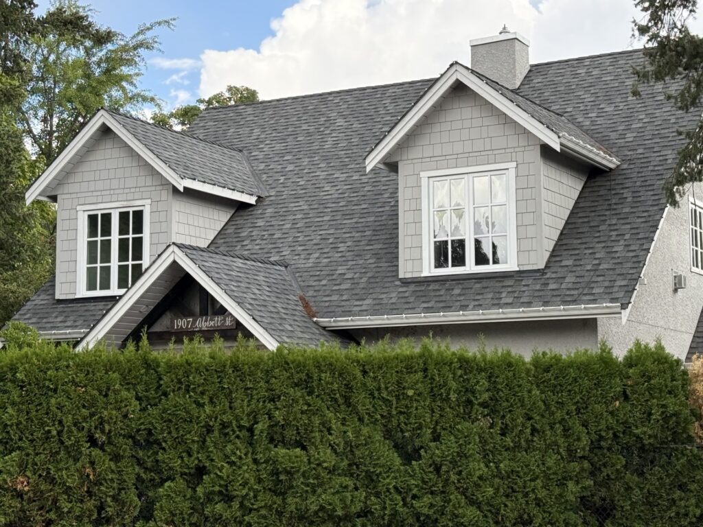 Grey shingle-clad dormers with white-trimmed windows above stucco walls at 1907 Abbott Street in Kelowna’s Heritage Conservation Area.
