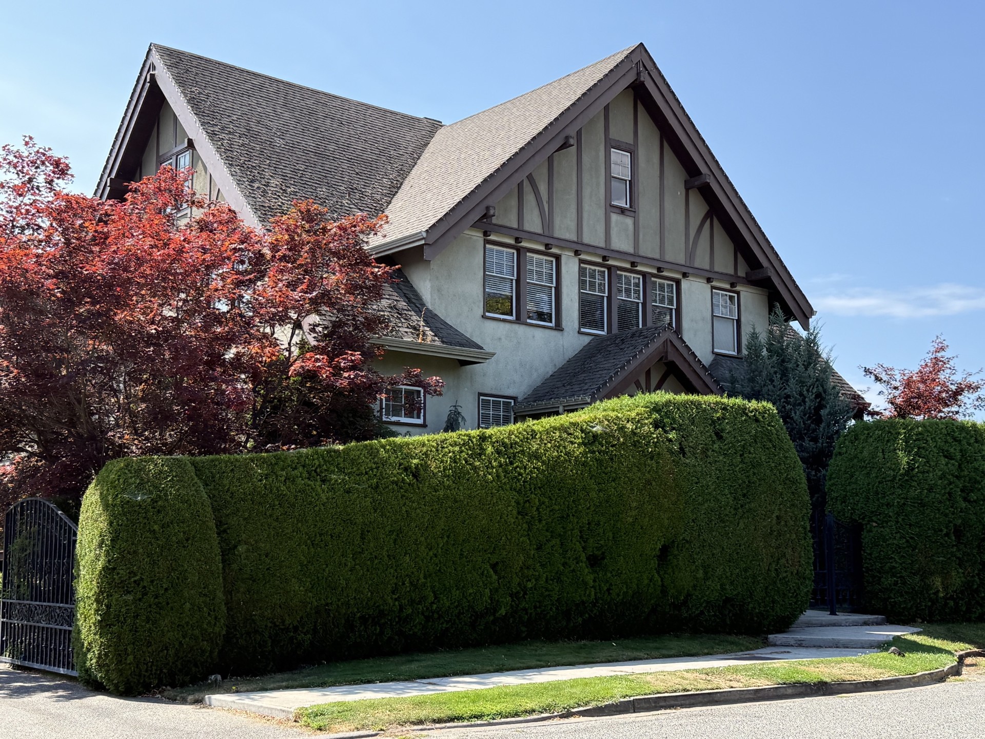 Steep-gabled home at 273 Burne Avenue in Kelowna, framed by red-leaf trees and a tall green hedge.
